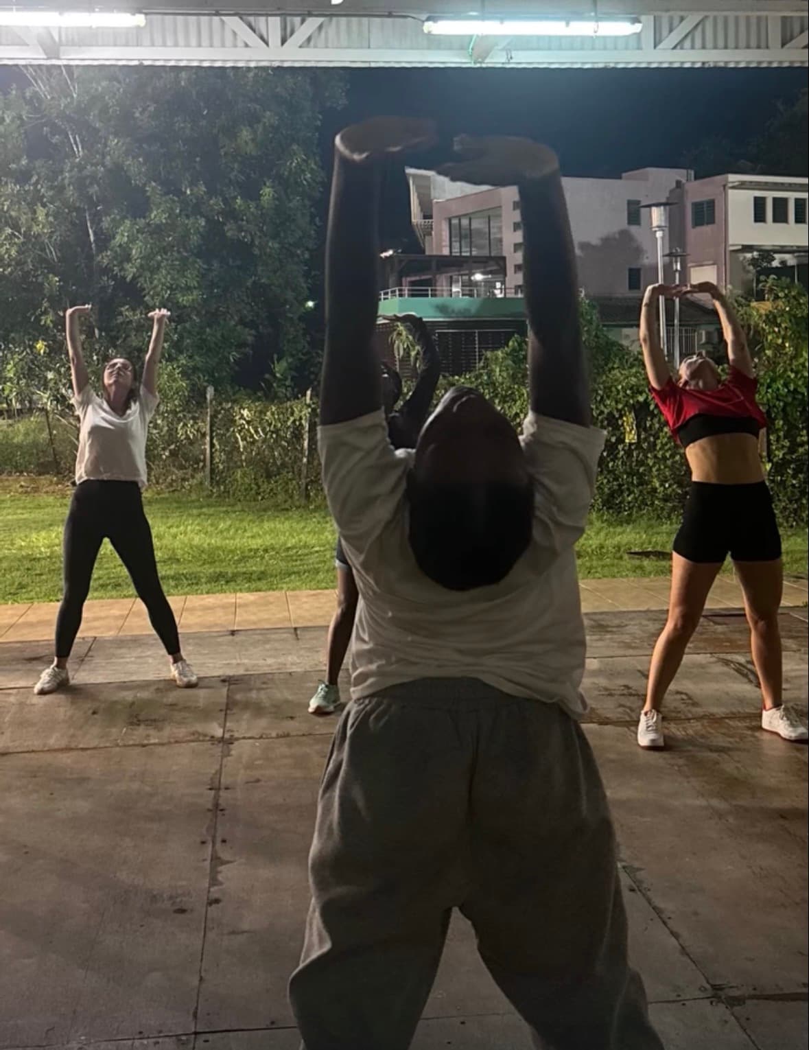 Groupe de personnes étirant leurs bras vers le haut lors d'une séance de sport nocturne.