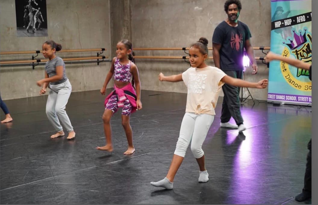 Trois jeunes filles pratiquent des mouvements de danse dans un studio avec leur instructeur.