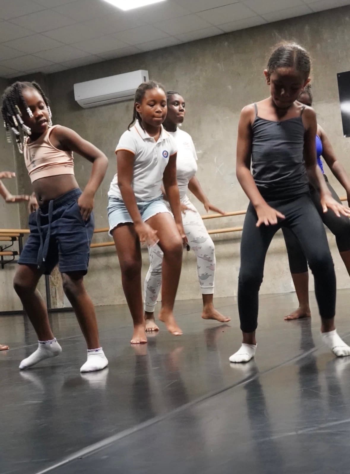 Jeunes filles pratiquant une chorégraphie dans un studio de danse aux murs en béton.